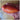 A hand holding a red speckled Roman tomato with wavy orange stripes.